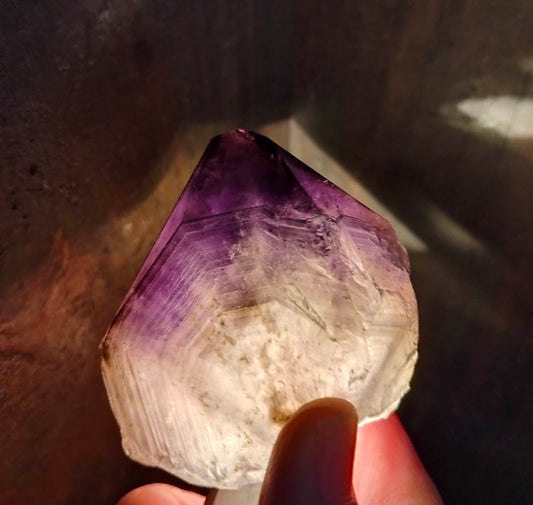 Amethyst crystal point with pyrite and hematite inclusions held by a hand against a dark background