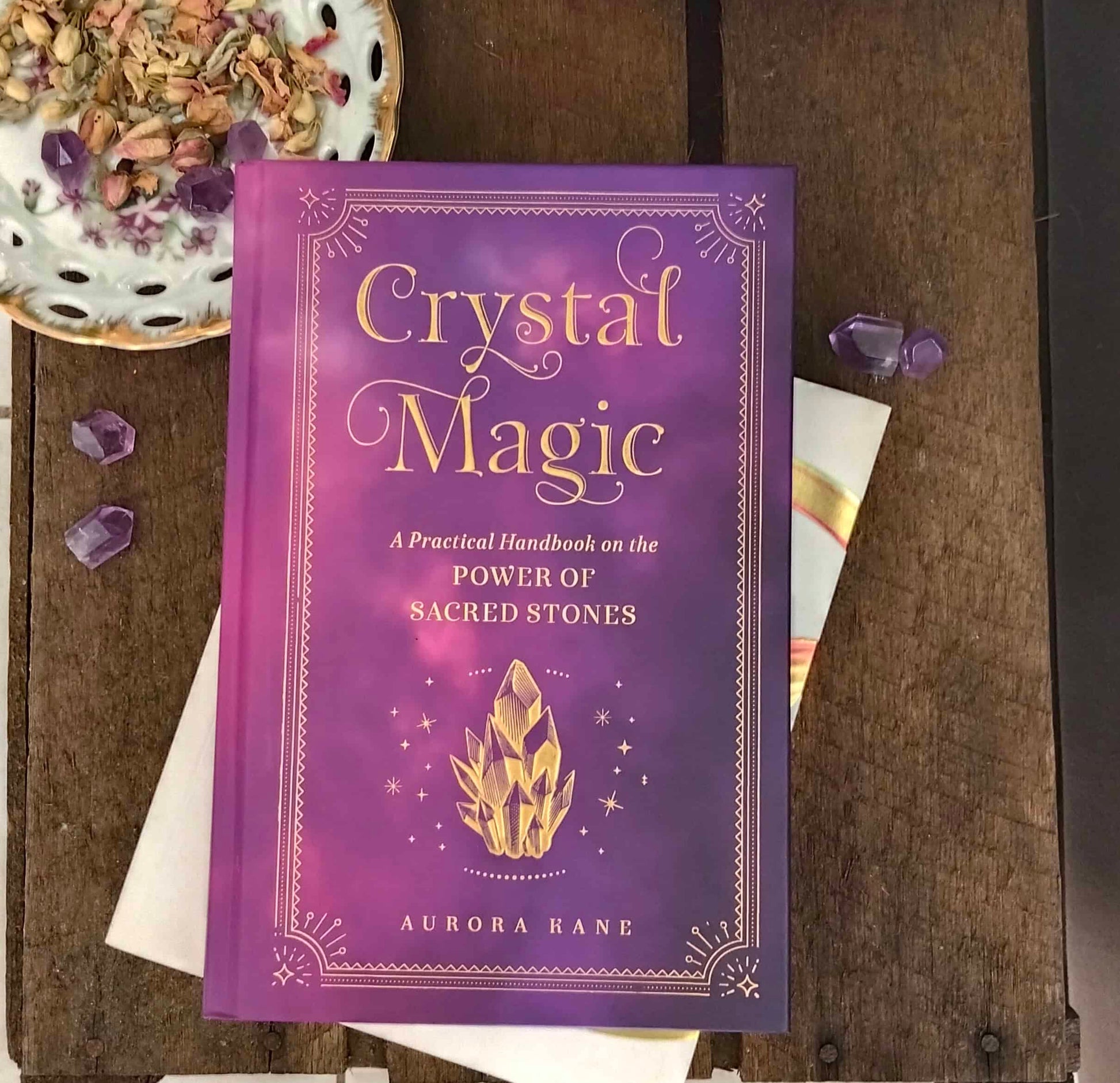 Purple book titled 'Crystal Magic' on a wooden surface with crystals around