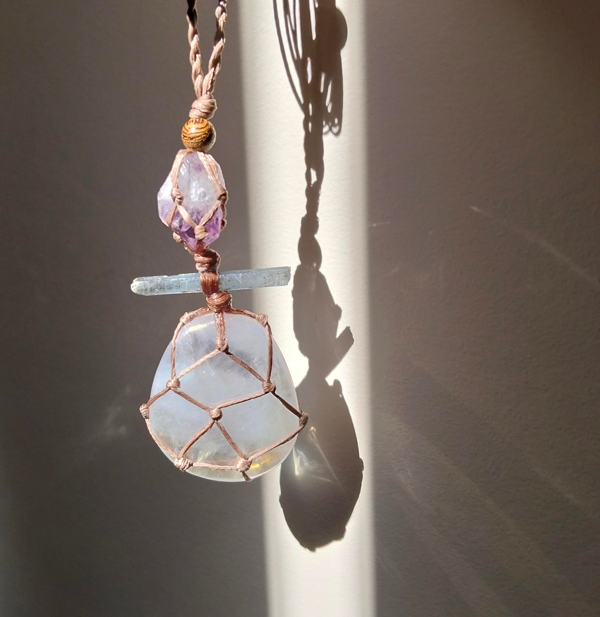 Necklace with a pendant featuring a large  rose aura quartz pendant smaller kyanite crystal amd amethyst gemstones with a hand made twisted leather chord