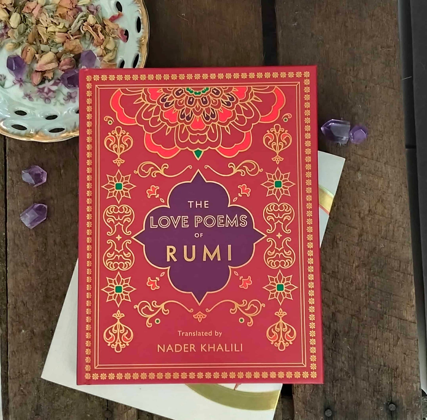 Book titled 'The Love Poems of Rumi' on a wooden surface with decorative elements.