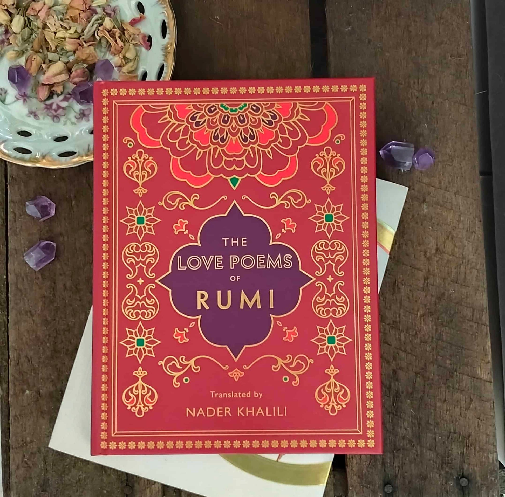Book titled 'The Love Poems of Rumi' on a wooden surface with decorative elements.