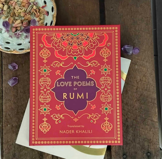 Book titled 'The Love Poems of Rumi' on a wooden surface with decorative elements.